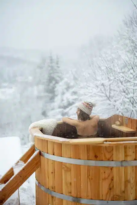 Eine Frau im Whirlpool vor einem Wellness Baumhaushotel im Winter